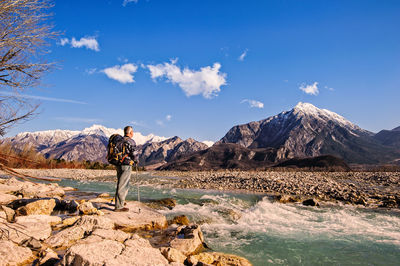 Rear view of man standing by river against mountains 