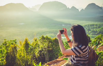 Close-up of woman photographing through mobile phone while sitting on mountain