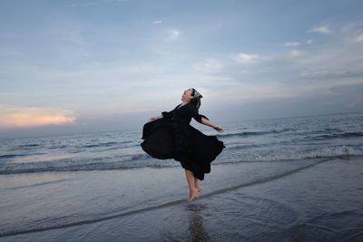 Rear view of woman standing at beach against sky during sunset