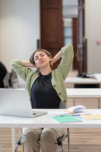 Tired female mature student taking break stretching arms while studying online in university library