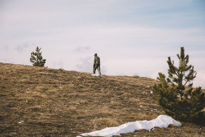 Rear view of man walking on hill against sky