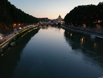 River amidst illuminated city against sky at dusk