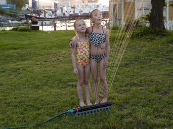 Girls standing near water sprinkler in garden