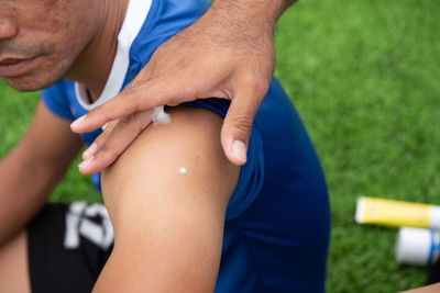 Cropped hands of male physical therapist applying ointment on soccer player shoulder at field