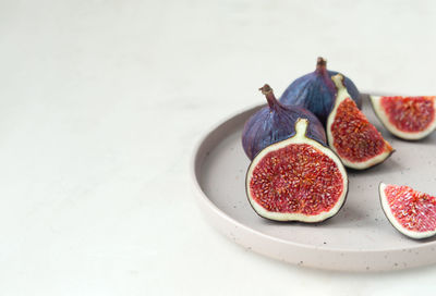 Fresh ripe figs whole and cut into slices on stylish beige ceramic plate on gray empty background
