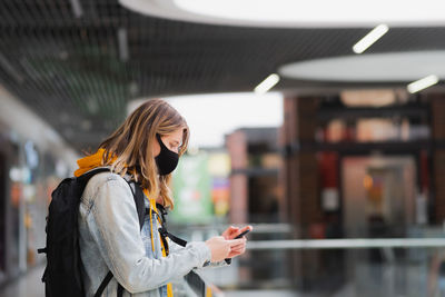 Woman in protective mask with cell phone at a shopping centre or