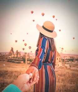 Cropped image of man holding hand of woman while standing on field against sky during sunset