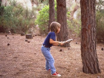 Full length of boy holding stick while standing in forest