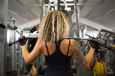 Rear view of woman with tattoo on back exercising at gym