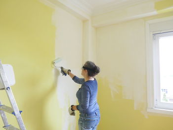 Woman painting a yellow wall white with a paint roller