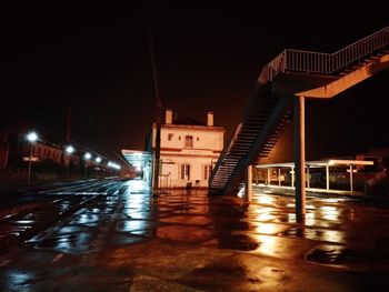 Illuminated bridge over wet street amidst buildings in city at night