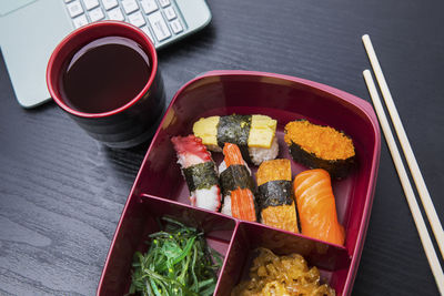 High angle view of sushi in lunch box by black coffee on table