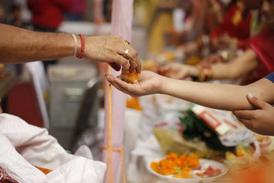 Cropped hand of priest giving sweet food to person at temple