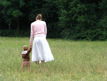 Rear view of mother with baby boy walking on grassy field