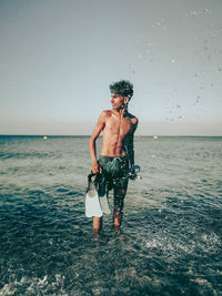 Full length of shirtless man standing in sea against sky