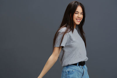 Portrait of young woman standing against gray background