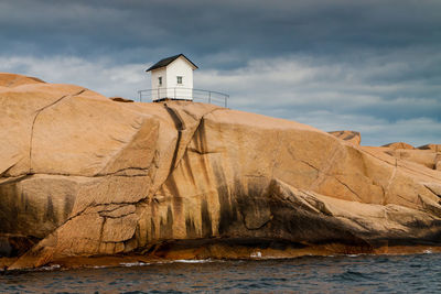 Hut on rock formation at sea shore against sky