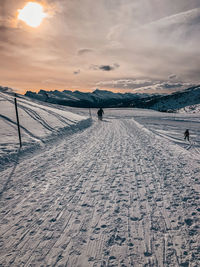 Person walking on snow covered mountain against sky during sunset