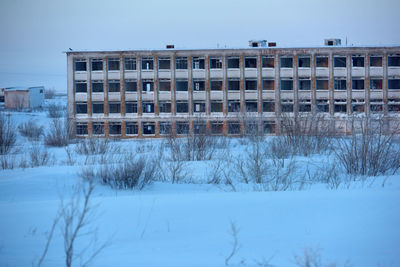 Snow covered field by building against sky