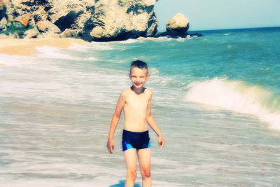 Full length portrait of shirtless boy standing at beach