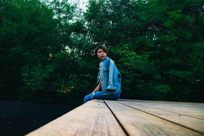 Portrait of woman sitting on wood against trees