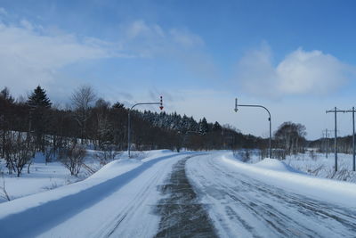 Snow covered road by trees against sky