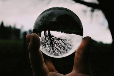 Close-up of person holding crystal ball against sky