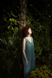 Woman in green dress leaning on a palm tree in the evening light in a park