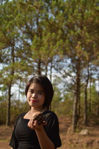 Portrait of young woman holding pine cone while standing on land