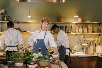 Young female chef preparing food with colleagues in commercial kitchen