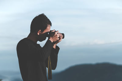 Portrait of young man standing on mountain against sky