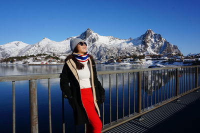 Portrait of young woman standing on snowcapped mountain against clear blue sky