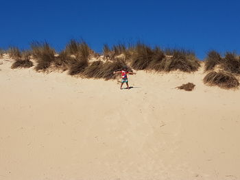 Man on sand dune in desert against clear blue sky