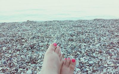 Low section of woman legs on pebbles at beach against sky