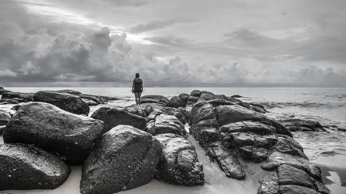 Man standing on rock by sea against sky