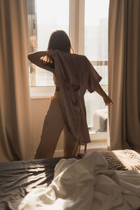 Rear view of woman sitting on bed at home
