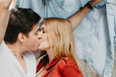 Young couple kissing under jacket against wall