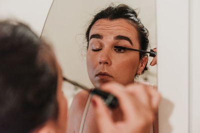 Mirror photo of beautiful young woman putting on makeup