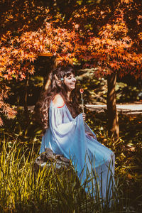 Young woman sitting against tree during autumn