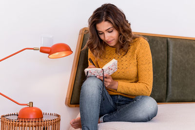 Smiling woman writing in diary while sitting on bed at home