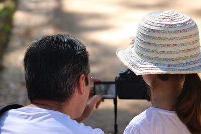 Rear view of father and daughter looking at digital camera