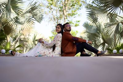 Young couple sitting on plant against trees