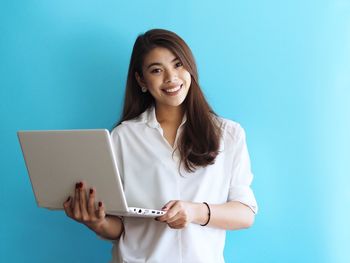 Portrait of smiling young woman using phone against blue background