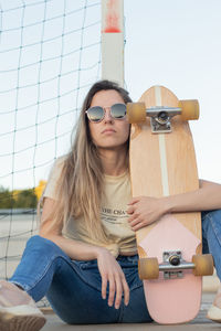 Front shot of a defiant blonde girl sitting on the floor next to her pink vintage skateboard