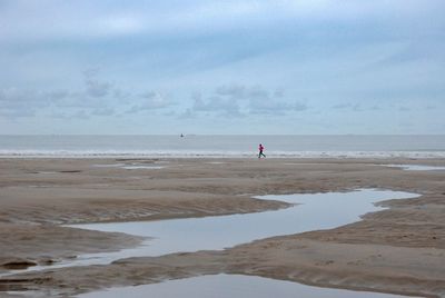 Rear view of woman walking at beach against sky