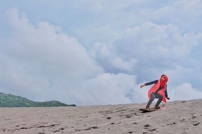 Low angel view of woman skateboarding on sand dune against sky