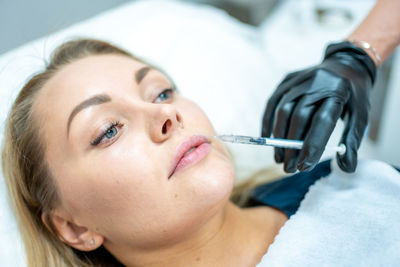 Cropped hand of beautician injecting collagen in patients face