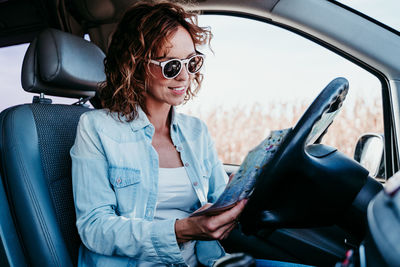 Smiling woman wearing sunglasses reading map in car