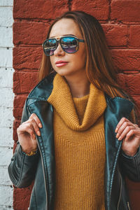 Young woman wearing sunglasses standing against wall