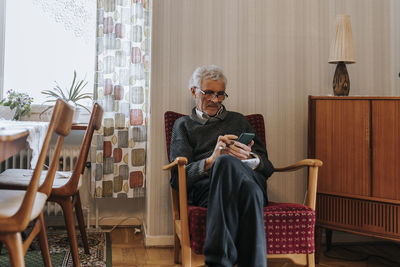 Senior man using smart phone while sitting on chair at home